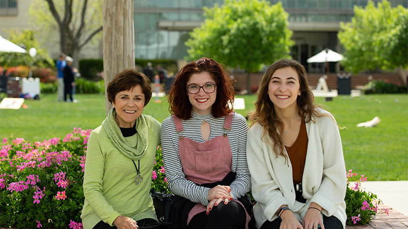 Outdoor photo of older woman seated and smiling with two young women